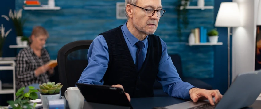 Senior business professional conducting doctoral research using a laptop and tablet