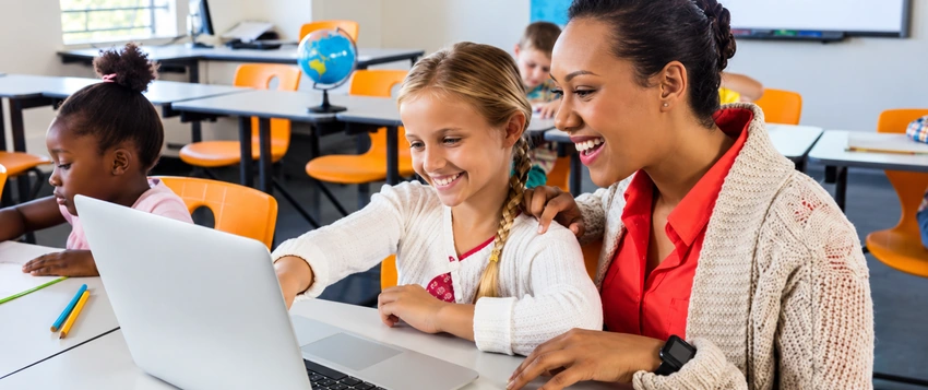 Teacher supporting a student using a laptop in a modern classroom, representing the future of education and digital learning