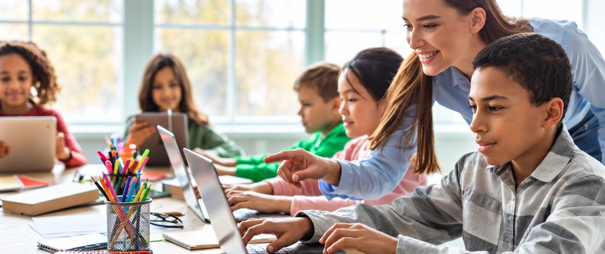 Teacher guiding students using a laptop in a modern classroom, representing human-centred learning and AI in education