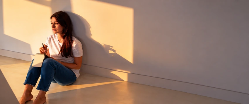 Woman sitting quietly in reflection, representing emotional suppression, fear of judgement and the psychology of silence
