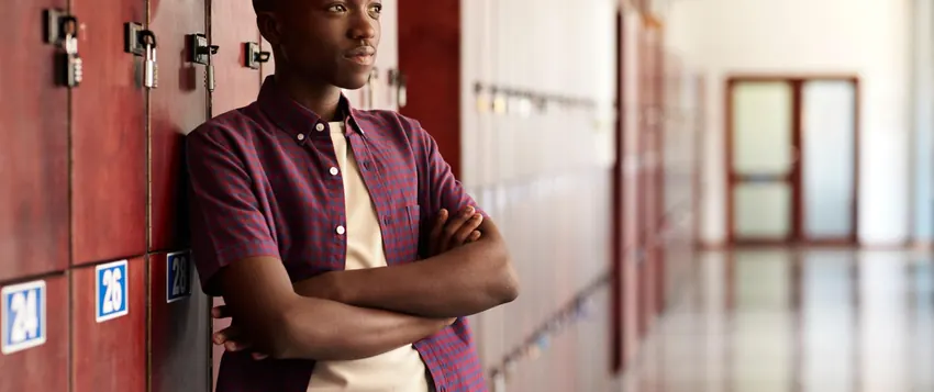 Black teenage boy standing thoughtfully beside school lockers, reflecting the emotional challenges and gender stereotypes affecting boys in South Africa